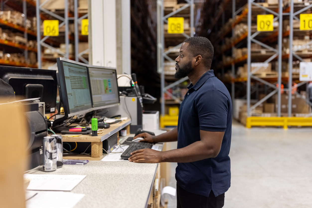 A Procurement Specialist Works on a Computer in a Warehouse.