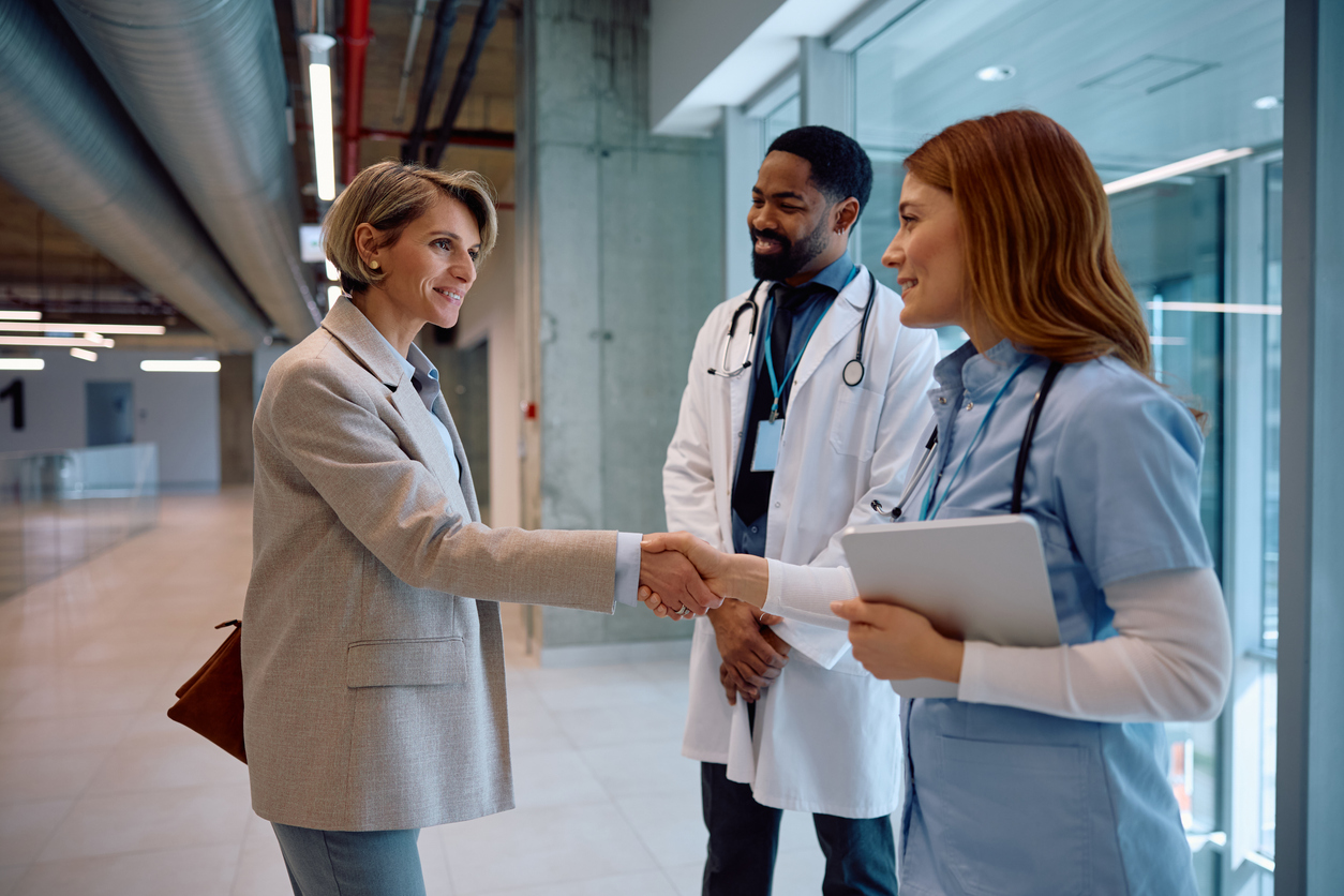 A health care administrator greets clinical care providers in a hospital corridor.
