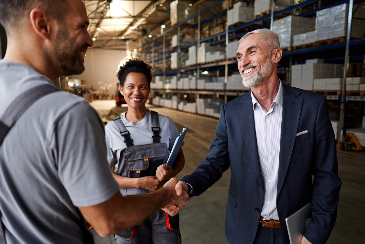 A smiling supply chain manager shakes hands with a warehouse worker.