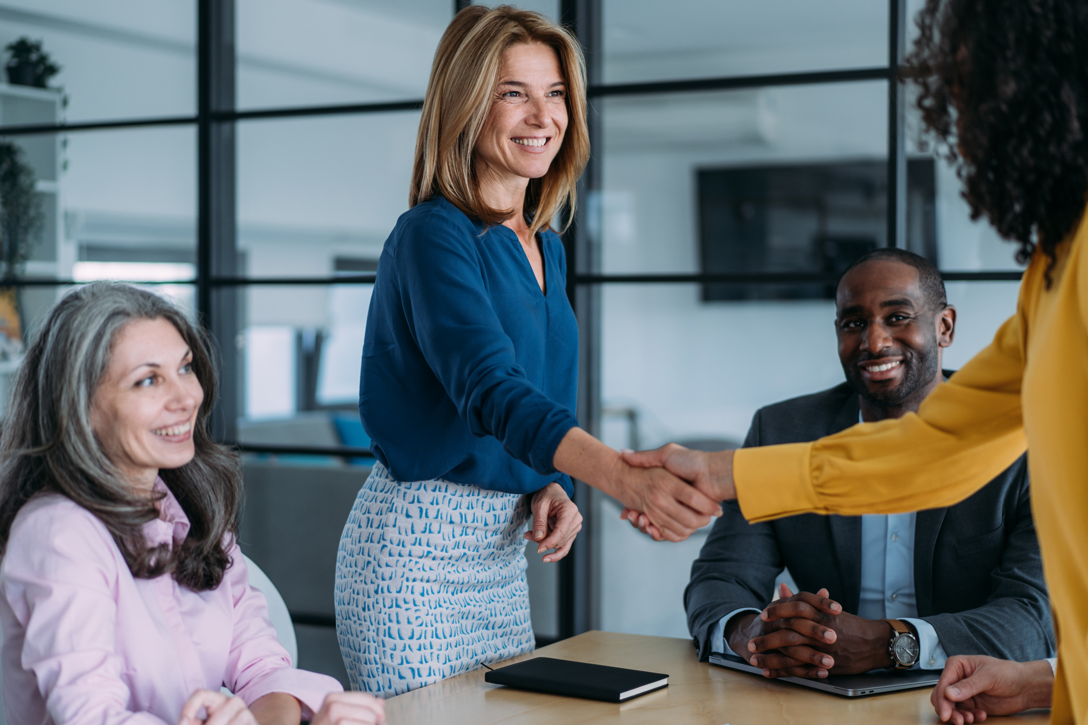 A business development representative shakes hands with a sales prospect across a conference table.