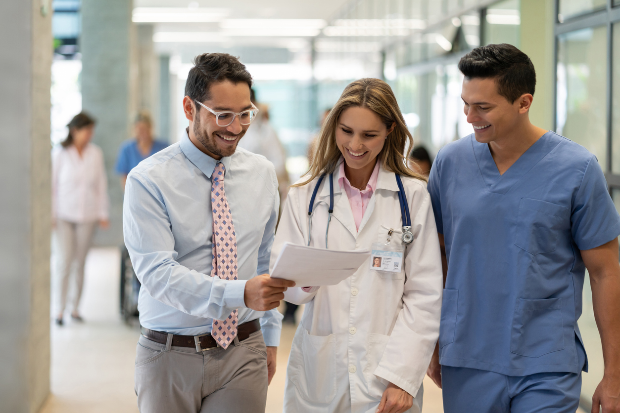 A health care administrator talks with two care providers in a hospital corridor.