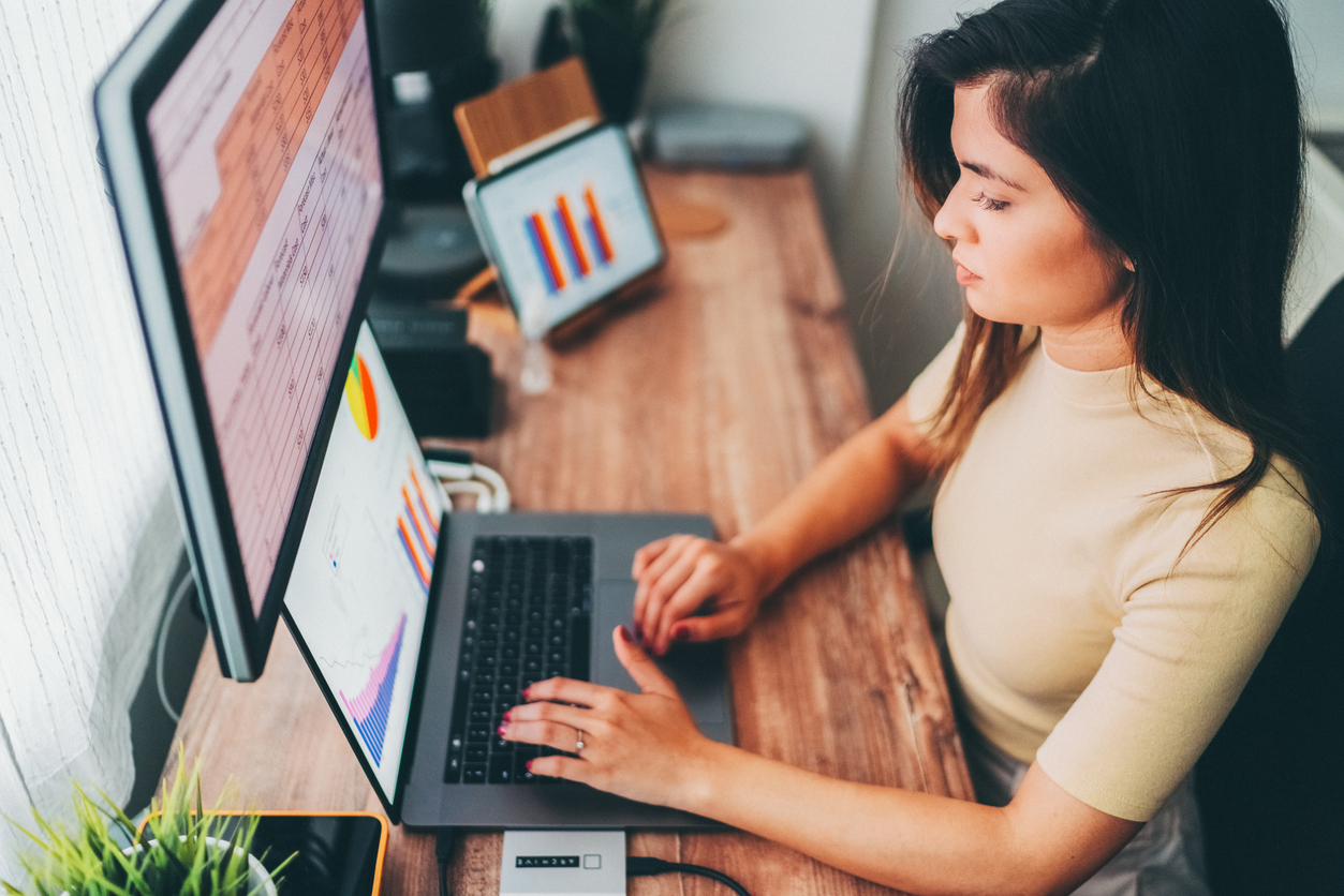 A financial analyst reviews data on a laptop and monitor.